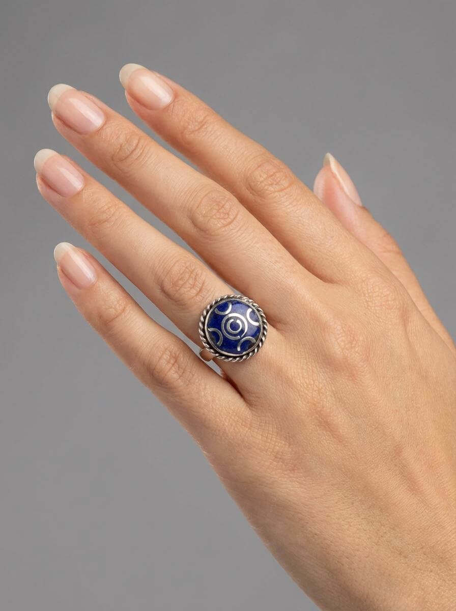 Hand wearing a ring with a blue gemstone on a gray background