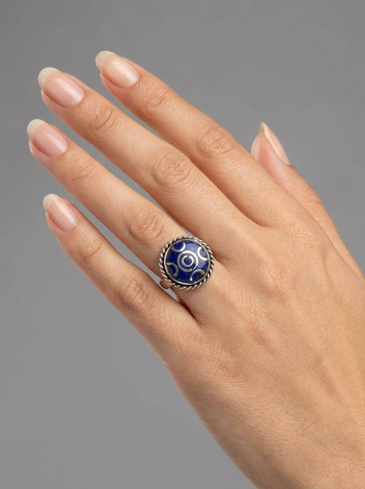 Hand wearing a ring with a blue gemstone on a gray background