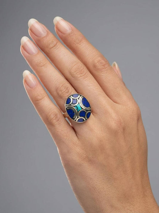 Hand wearing a ring with a blue and gold design on a gray background