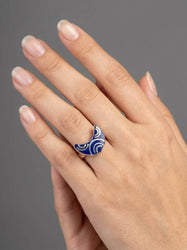 Hand wearing a blue and white patterned ring on a gray background