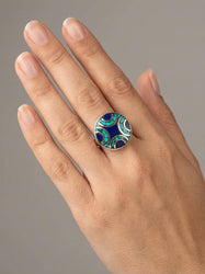 Hand wearing a ring with a blue and green circular design on a neutral background
