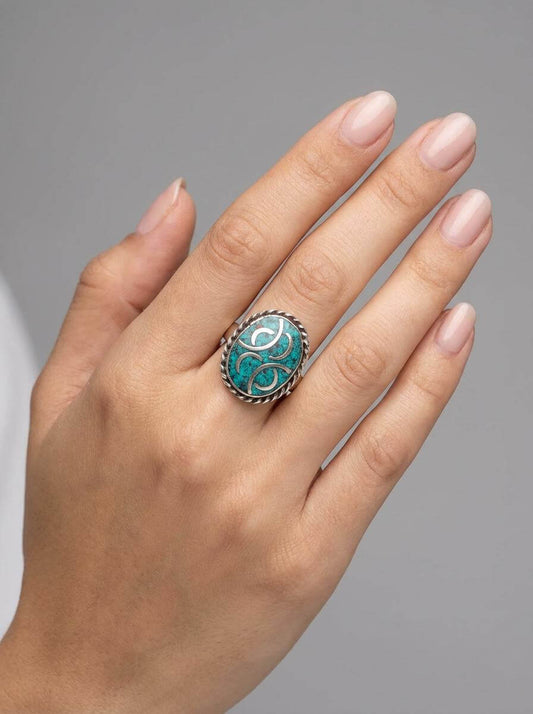 Hand wearing a ring with a turquoise stone on a gray background