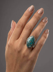 Hand wearing a decorative ring with a blue stone on a gray background